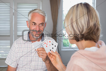 Smiling mature man playing cards with woman at home