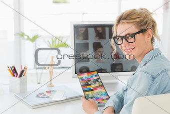 Blonde designer holding colour chart at her desk smiling at camera