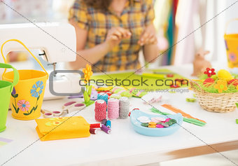 Closeup on threads and buttons on table and young woman making e