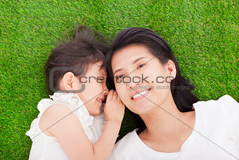 mother and daughter whispering gossip on the grass