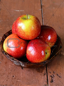 Red ripe apples in a wicker basket on a wooden table