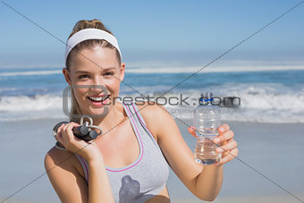 Sporty happy blonde standing on the beach with bottle and skipping rope