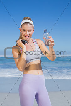 Sporty happy blonde standing on the beach with water bottle and skipping rope