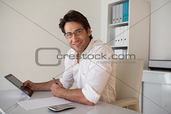 Casual smiling businessman using tablet and calculator