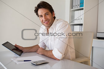 Casual smiling businessman using tablet and calculator