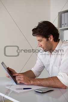 Casual focused businessman using tablet and calculator