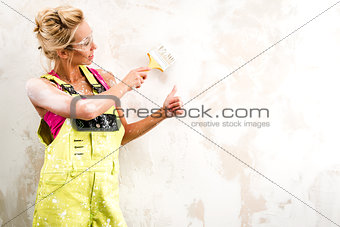 Female worker in coverall paint a  wall and showing thumbs up