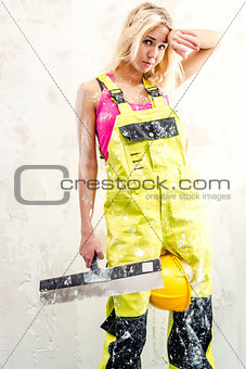Tired female construction worker with putty knife working indoor