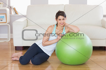 Fit brunette leaning on exercise ball smiling at camera