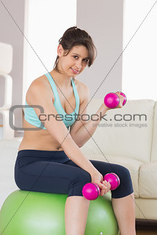 Fit brunette sitting on exercise ball lifting hand weights