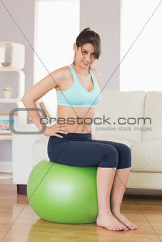 Fit brunette sitting on exercise ball smiling at camera