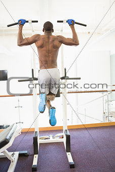 Rear view of body builder doing pull ups at gym