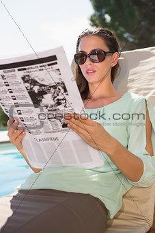 Woman reading newspaper on sun lounger by pool