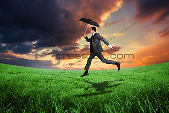 Composite image of businessman jumping holding an umbrella