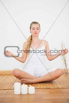 Peaceful blonde sitting in lotus pose on bamboo mat