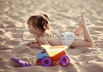 Adorable baby girl lying in the sand on the beach