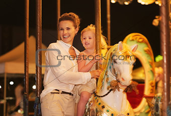 Happy mother and baby girl riding on carousel