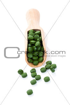 Green pills on wooden spoon isolated.