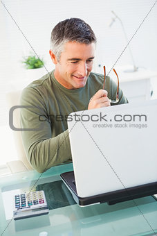 Smiling man holding glasses and using laptop