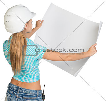 Beautiful woman builder holding in front of him large paper sheet. Rear view