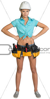 Pretty girl in helmet, shorts, shirt and tool belt with tools. Full length