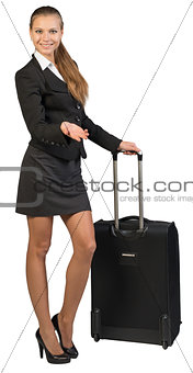 Businesswoman with wheeled suitcase, showing something, looking at camera, smiling