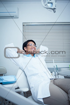 Female dentist sitting on chair with hands behind head