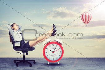 Businesswoman sitting with her feet up on alarm-clock 