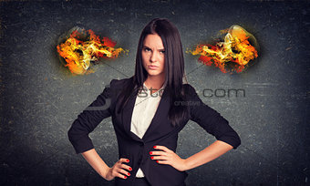 Angry woman standing with arms akimbo, fire from ears. Concrete wall in background