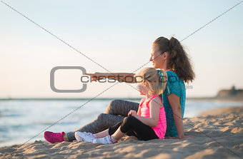 Baby girl and mother pointing while sitting on beach in the even