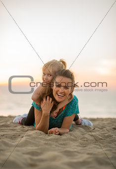 Happy mother and baby girl laying on beach in the evening