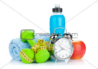 Two green dumbells, tape measure, healthy food and alarm clock