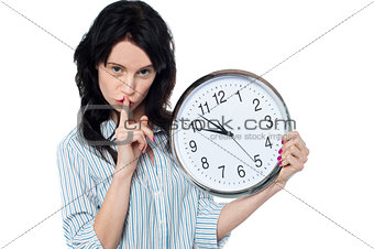 Young brunette with wall clock gesturing silence