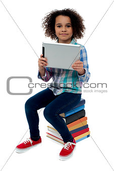 Adorable kid with tablet pc sitting on books