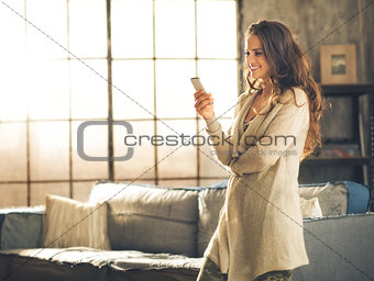 Woman looking away holding phone standing in loft apartment