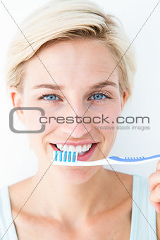 Happy blonde looking at camera holding toothbrush
