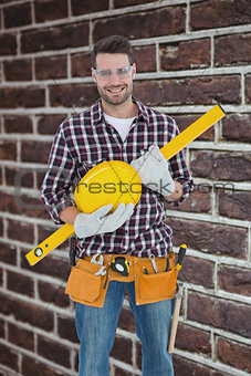 Composite image of handyman holding hard hat and spirit level
