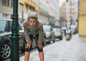 Woman runner in the rain taking a break and stretching