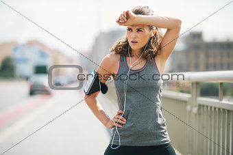 Woman jogger taking a break on bridge while wiping forehead
