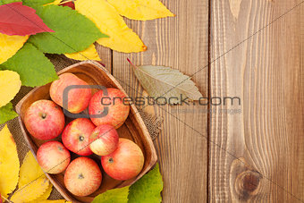 Apples in bowl and colorful autumn leaves on woden background