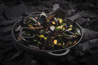 Steamed Mussels with vegetables in a black frying pan on the coa