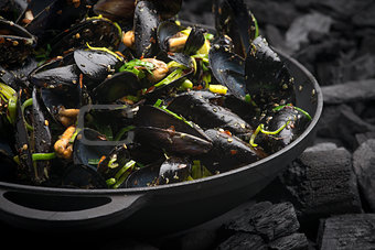 Steamed Mussels with vegetables in a black frying pan on the coa
