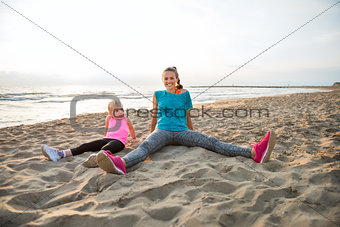 Happy fit mother and daughter sitting on the beach, relaxing