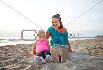 Fit, happy young mother and daughter in workout gear on beach