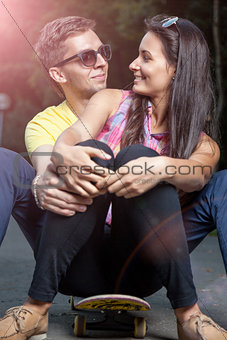 Young couple in love sitting on a skateboard outdoors
