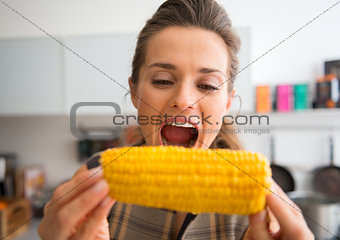 Closeup of woman opening mouth wide to take bite of corncob