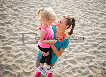 Young mother holding daughter in arms and smiling on the beach