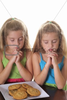 shot of two girls praying over cookies