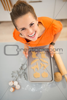 Smiling housewife holding tray of uncooked Halloween biscuits