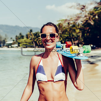 sexy suntanned lady with the blue penny board walks along the be